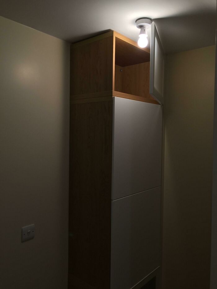 A DIY fail showing a kitchen light fixture installed directly above a tall cabinet, blocking the light.