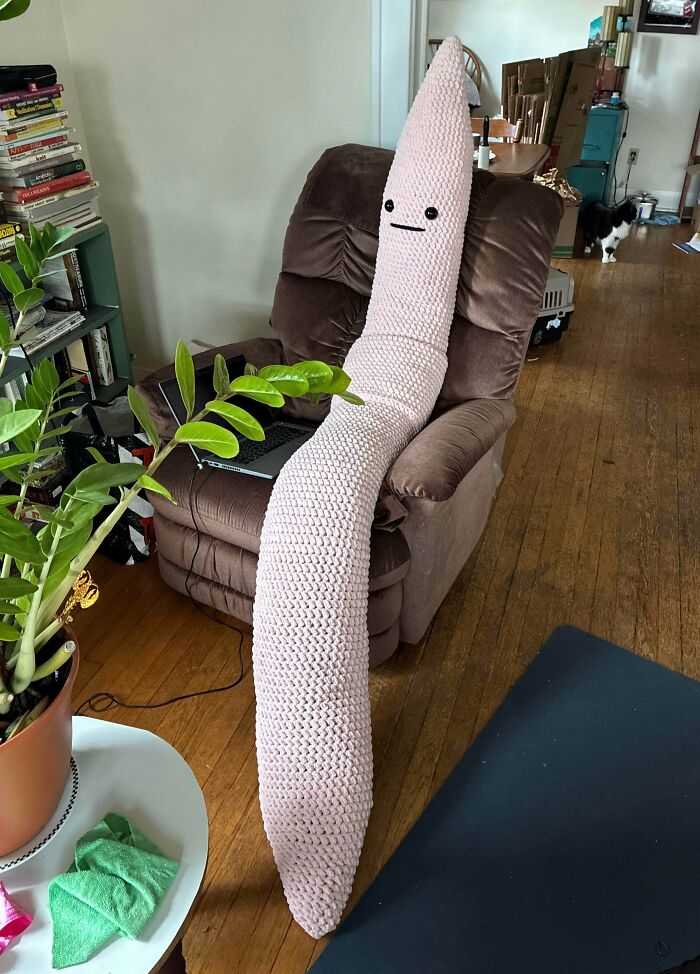 Large crocheted plush worm toy with face sitting on armchair