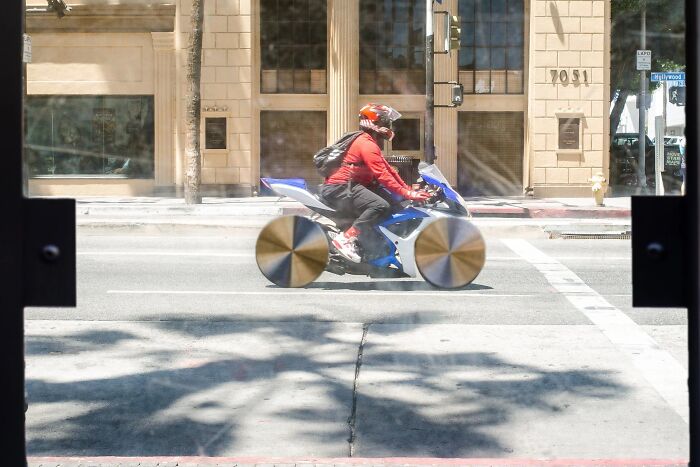 Perfectly timed street photo by Jeremy Paige of a person riding a motorcycle with unusual, shiny wheels.