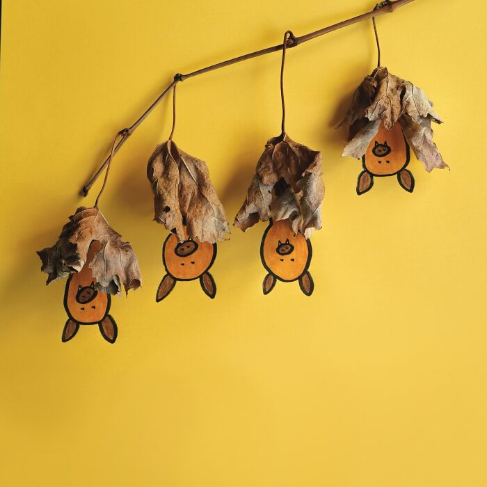 Playful illustrations of dried leaves turned into hanging bats on a yellow background