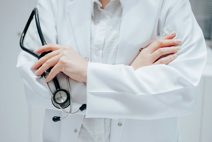 Medical professional in white coat holding stethoscope with crossed arms
