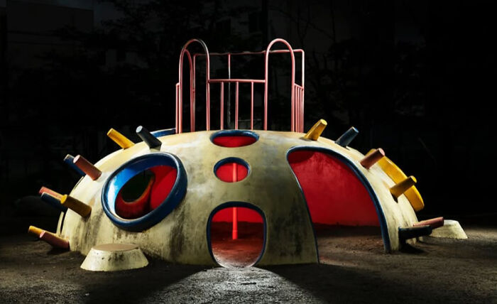 A unique, domed Japanese playground structure with multiple entrances and red lighting, captured at night by Fujio Kito.