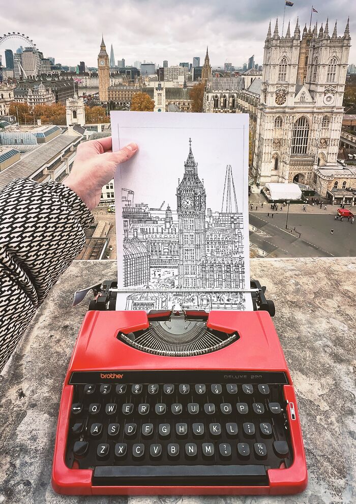 Hand holding a black and white typewriter art drawing of a city skyline over a red typewriter with the real skyline in the background.