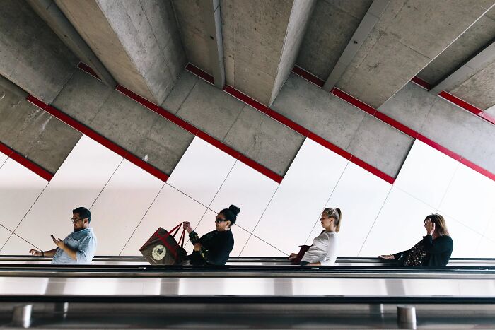 People sitting on an escalator, creating a perfectly timed street photo by Jeremy Paige with a diagonal architectural background.