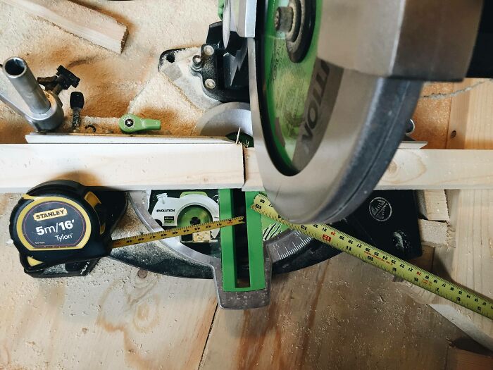 A miter saw with a measuring tape positioned precariously close to the blade, showing a DIY fail.