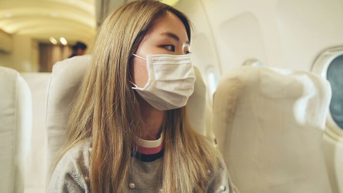 A young woman wearing a face mask on a plane, likely dealing with entitled people.