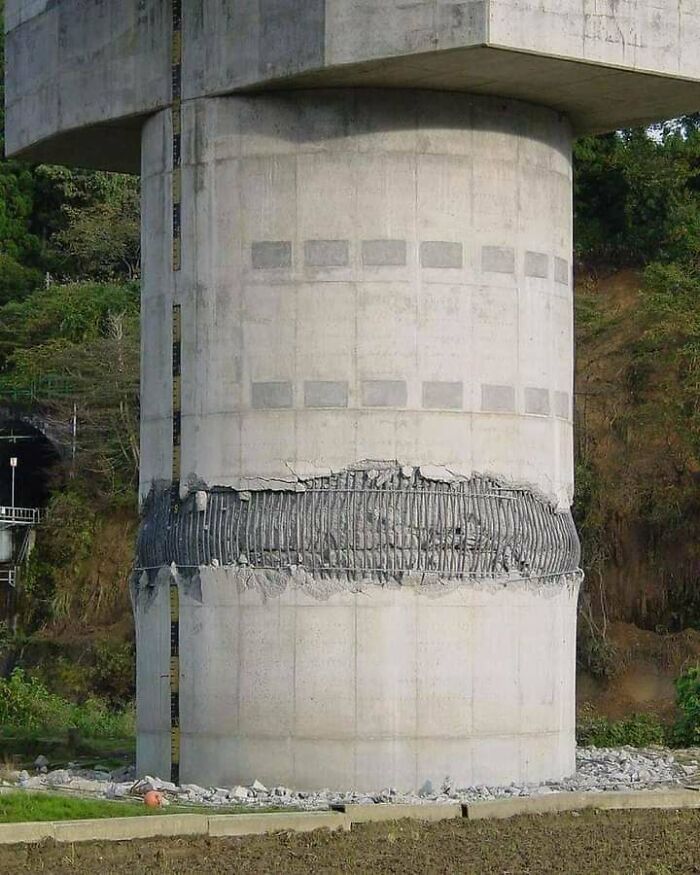 A severely damaged bridge column with exposed rebar, a bizarre sight showing infrastructure failure.