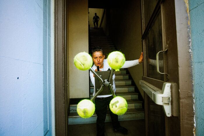Perfectly timed street photo by Jeremy Paige of a person holding a tennis ball contraption in a doorway.