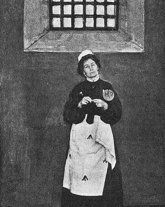 A black and white photo of a woman in a uniform, a dedicated suffragette among Women in History, standing in a jail cell, symbolizing her fight for women's rights.