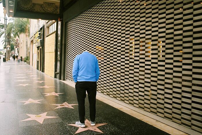 Perfectly timed street photo by Jeremy Paige of a headless person in a blue sweater on a sidewalk with stars.