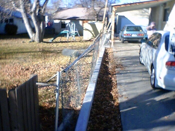A leaning chain-link fence separating a yard from a driveway, an obvious DIY fail of poor fence installation skills.