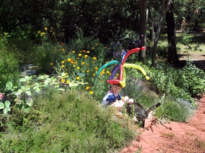 A child wearing a balloon hat in a garden, illustrating children's unique experiences parents might overlook.