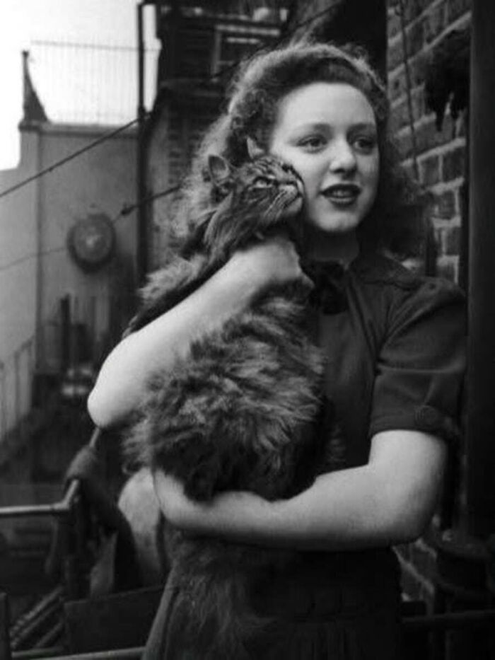 Vintage cat photo of a young woman smiling and holding a large fluffy cat close to her face on a balcony