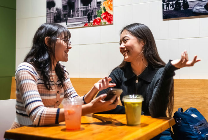 Two women enjoying a lively conversation over drinks in a cozy cafe setting