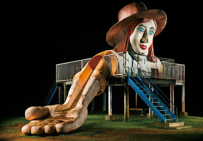 Surreal Japanese playground at night featuring a giant woman figure with a slide emerging from her arm by Fujio Kito.