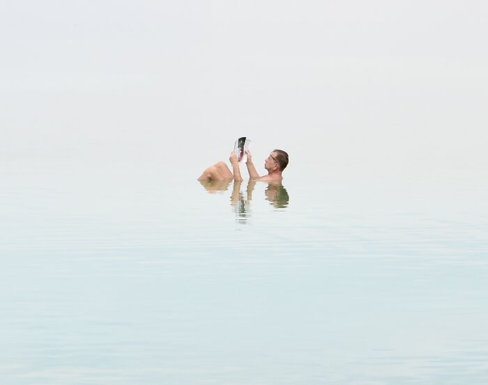 A photographer uses negative space to capture a person relaxing in water on a minimalist beach scene.