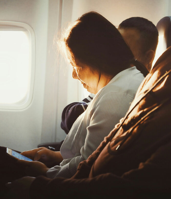 A woman on an airplane looking at her phone, depicting entitled people getting a reality check.