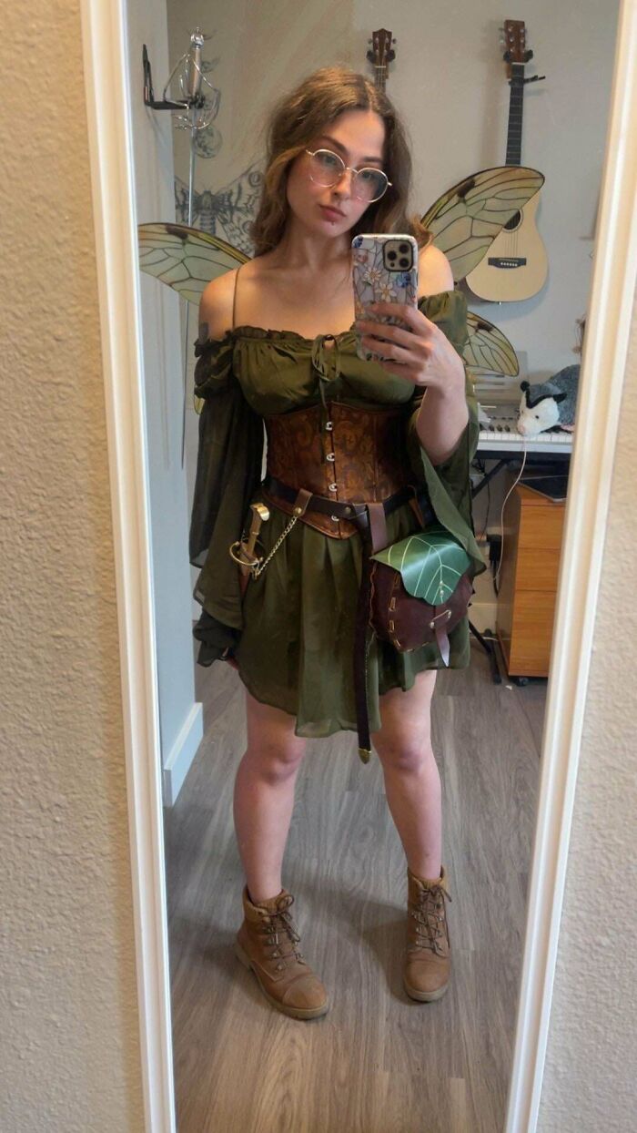 Woman in green fairy costume with wings and leaf bag taking mirror selfie