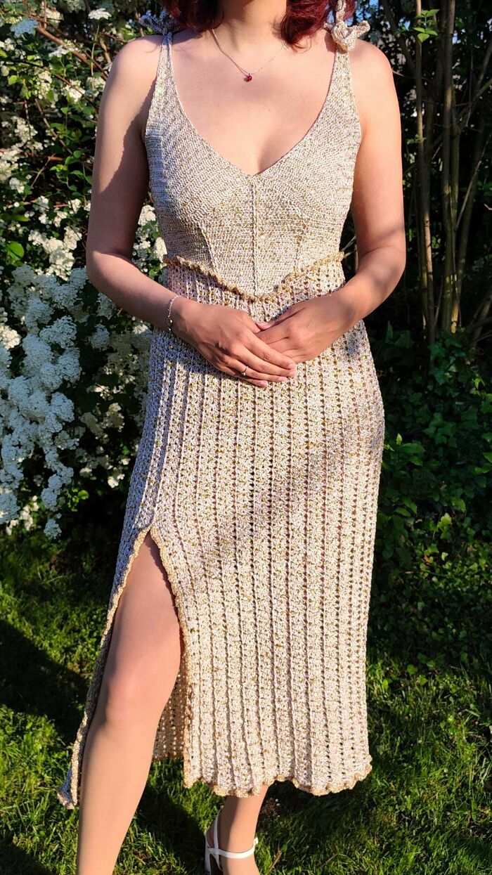 Crocheted gold dress with slit worn outdoors near white flowers