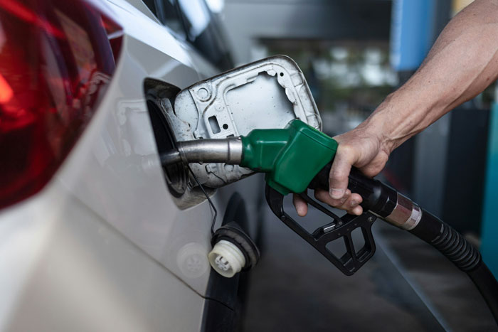 Hand holding green fuel nozzle refueling a white car at gas station