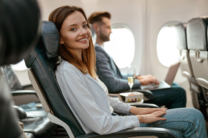 A smiling woman in an airplane seat, ready for a pleasant flight experience after winning the airline seating lottery.
