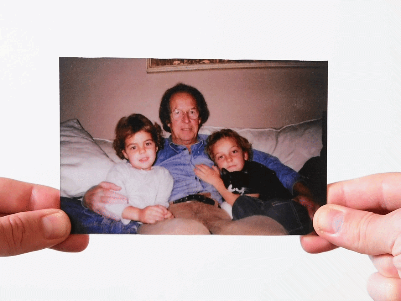 Photo of father with two children on a couch with a black and white cat