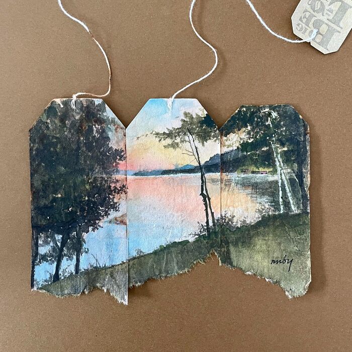 A serene lakeside landscape miniature painting across three used tea bags by artist Ruby Silvious