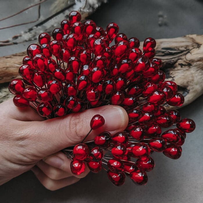 A hand holds a bunch of small, shiny, red-beaded decorative berries. These are forbidden foods.