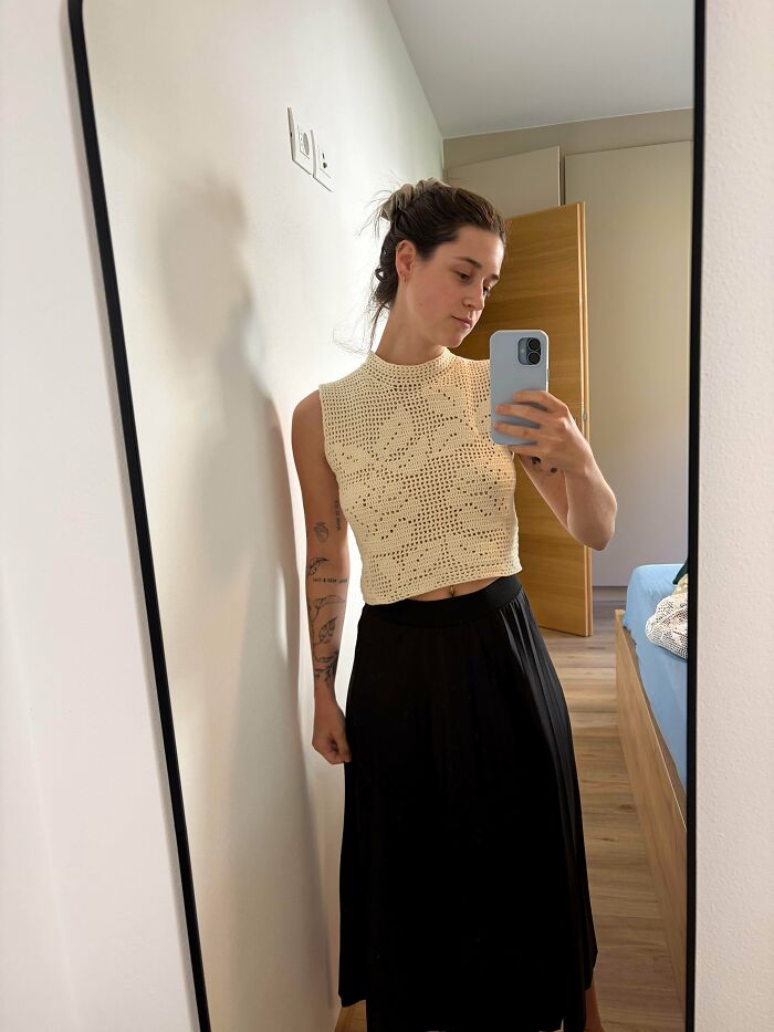 Woman wearing a handmade crochet crop top, taking mirror selfie indoors