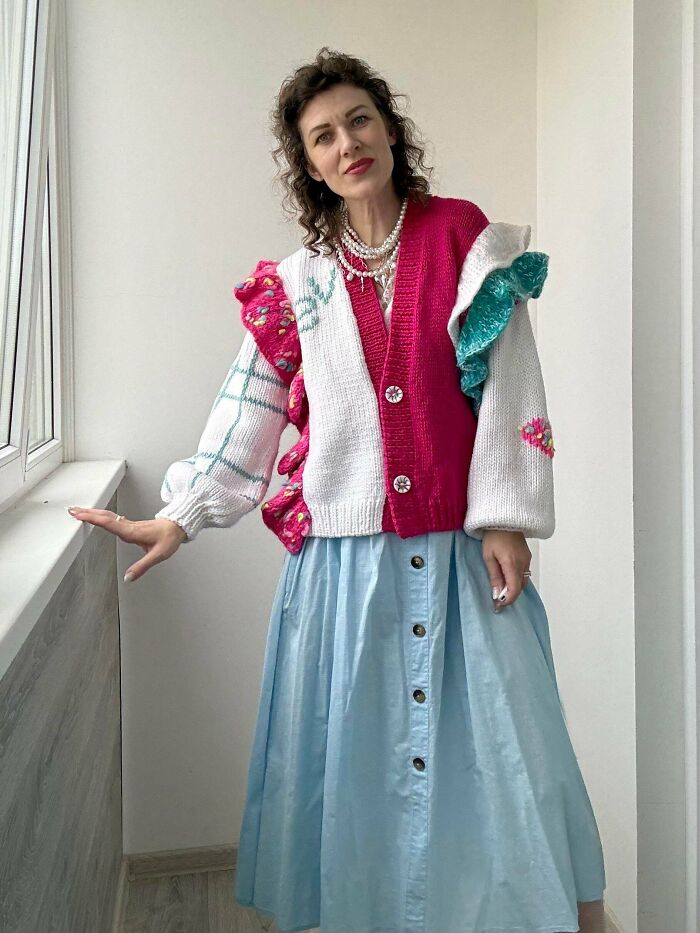 Person wearing quirky colorful knitted cardigan with ruffle details by window