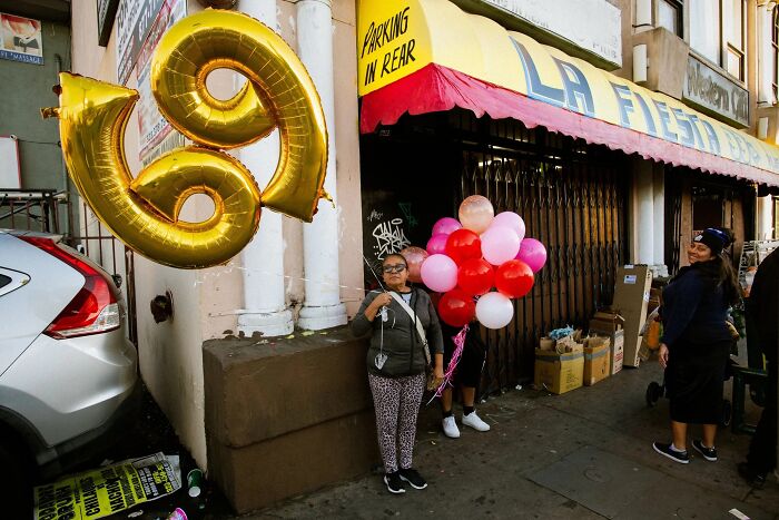 Perfectly timed street photo by Jeremy Paige of people with balloons, including large gold number 69 balloons.