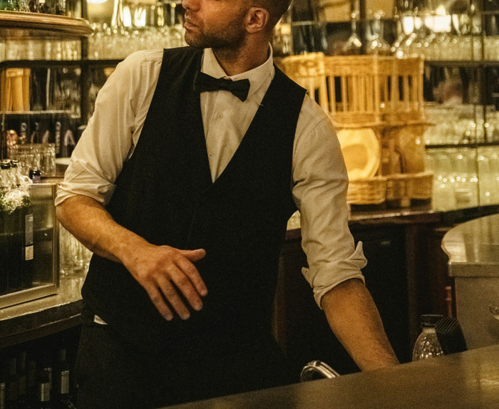 Bartender in formal attire preparing drinks behind a bar counter