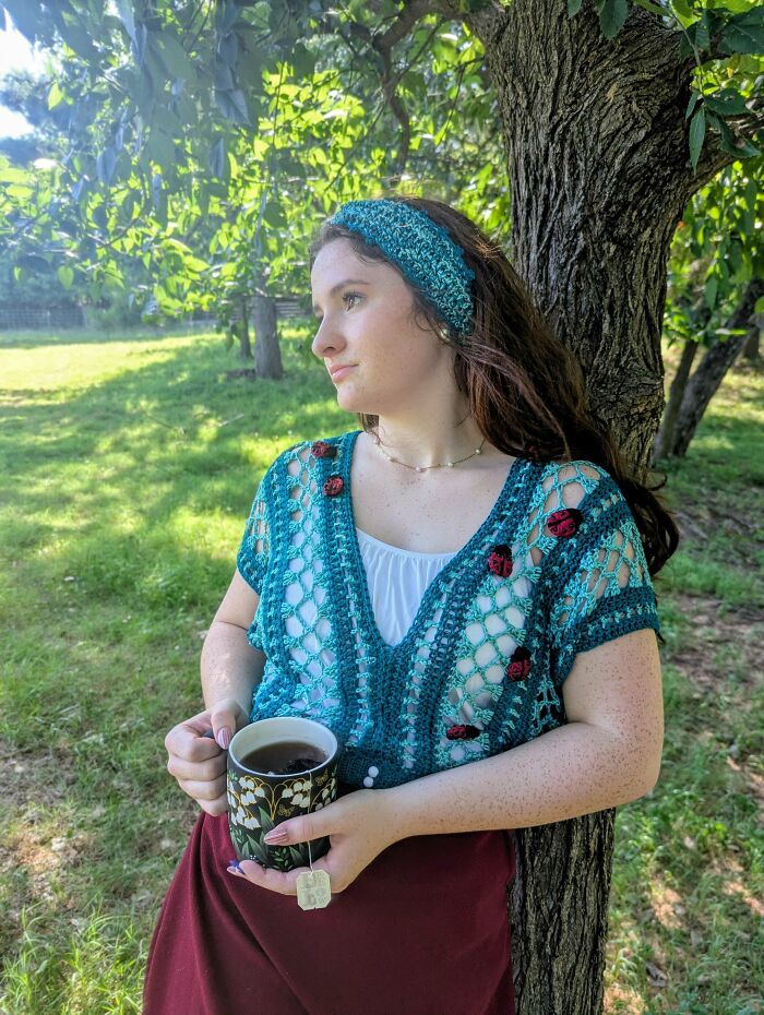 Woman wearing crochet outfit with ladybug details holding a cup outdoors