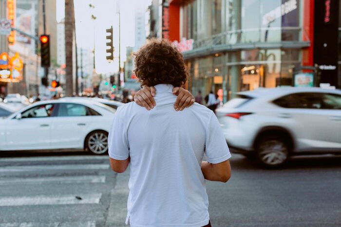 From behind, a man's hands appear to be around another man's neck on a city street, a perfectly timed photo by Jeremy Paige.