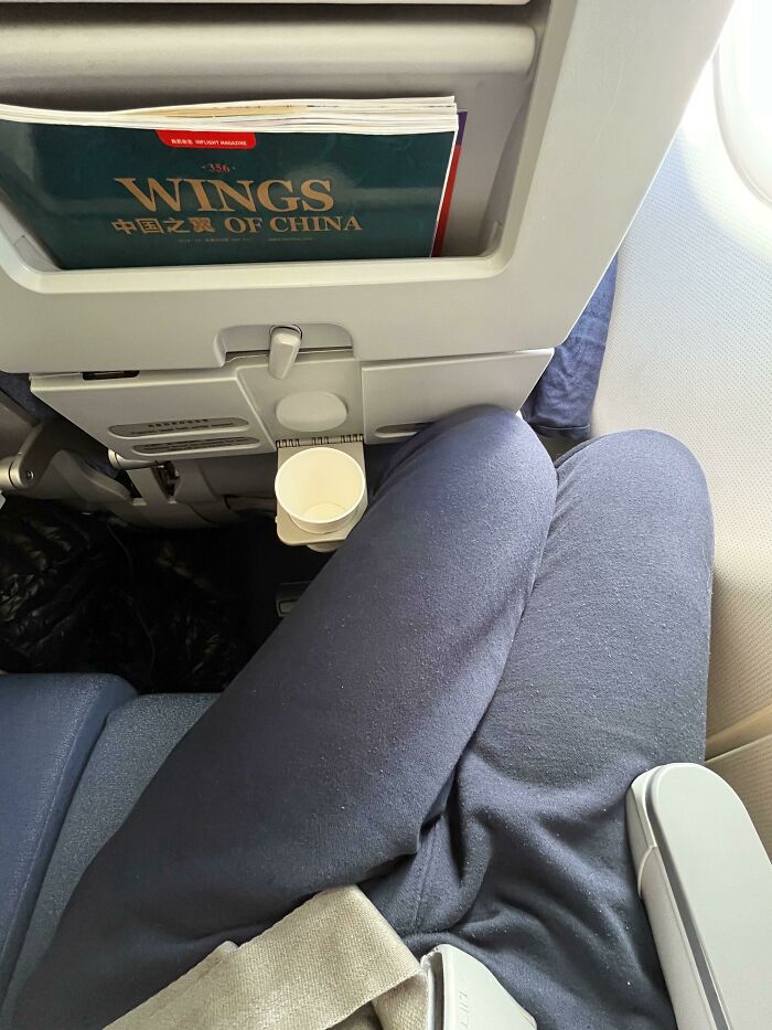 A passenger showing a lack of legroom on a flight, experiencing a reality check at 30,000 feet.