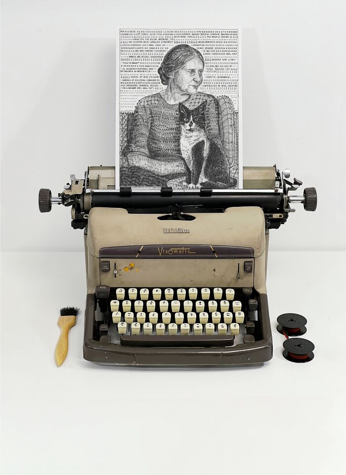 Vintage typewriter with a sheet of Typewriter Art showing a woman holding a cat, alongside typing accessories.