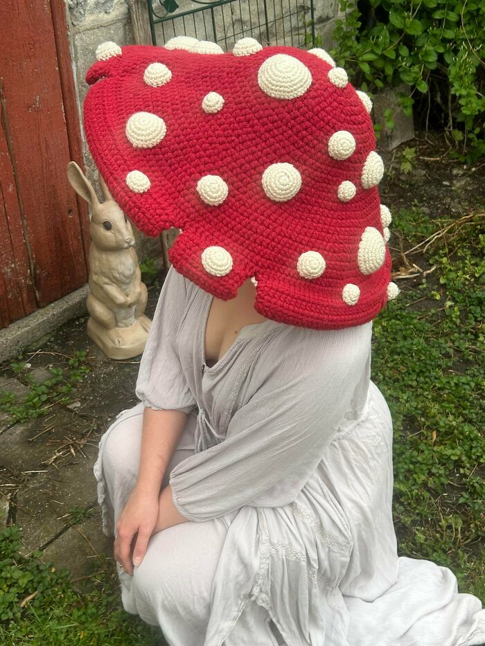 Person wearing a large red crocheted mushroom hat with white spots outdoors