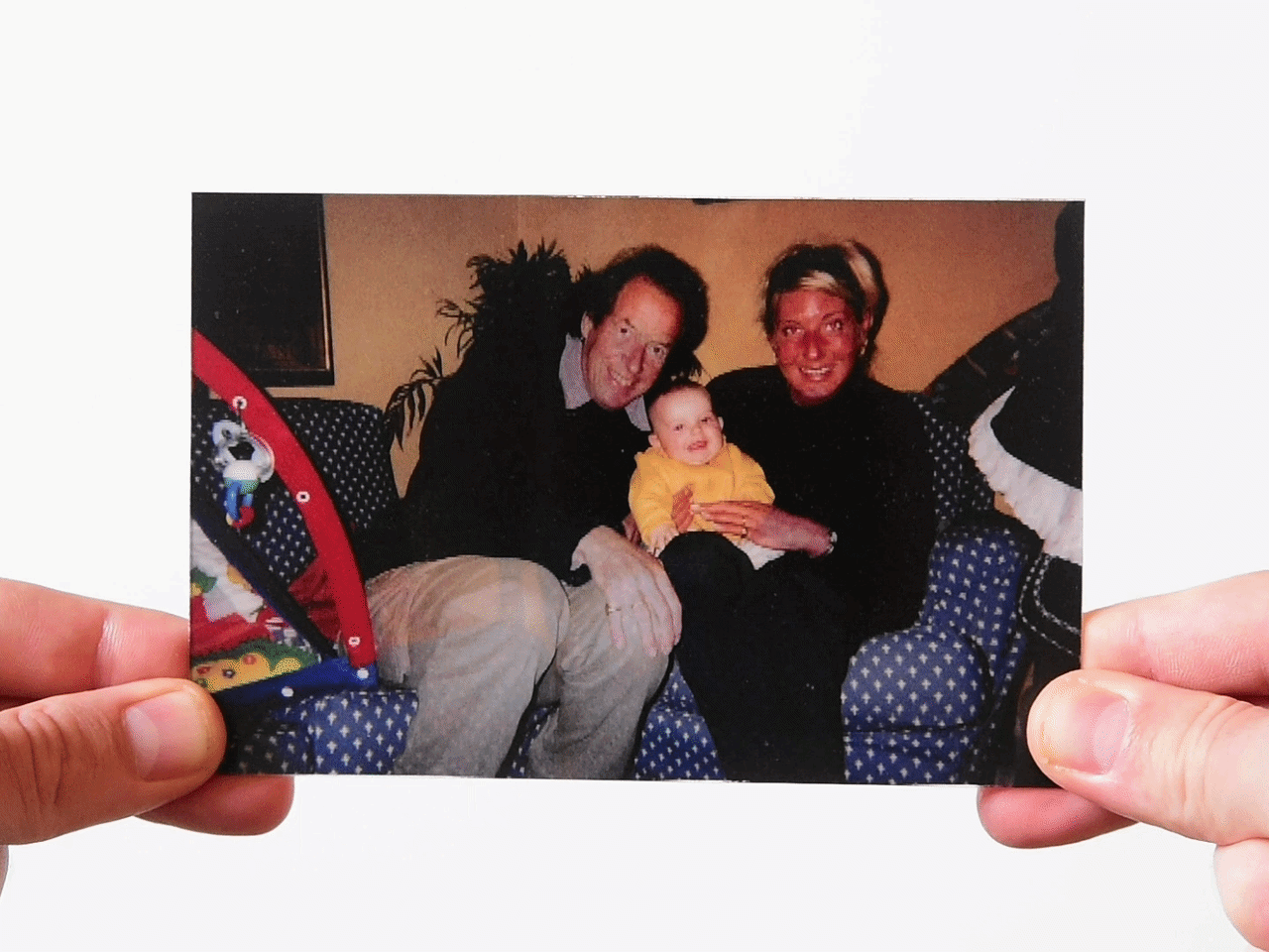 Photo of a smiling couple holding a baby on a blue couch indoors