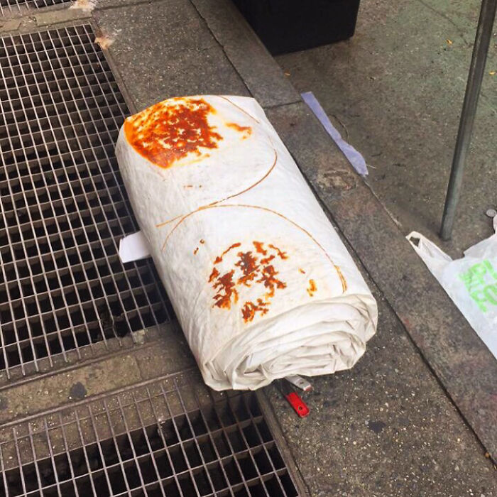 A giant burrito-like object on a street grate, resembling a strange and forbidden food.