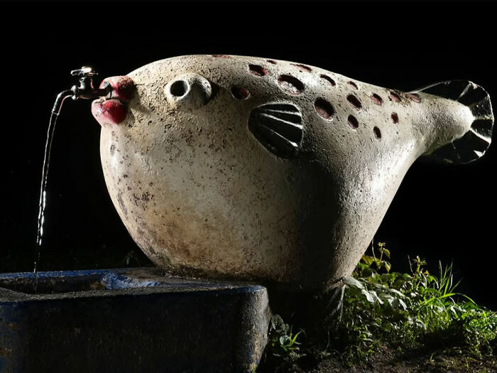 Surreal Japanese playground at night featuring a pufferfish fountain with water pouring from its mouth, captured by Fujio Kito.