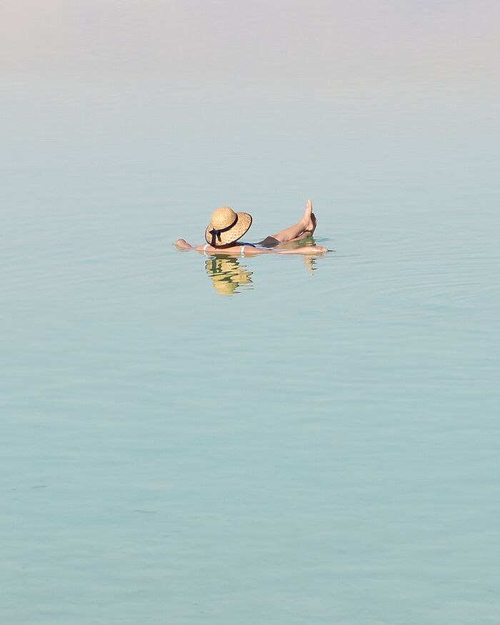 Person in a straw hat floating serenely in clear blue water, minimalist art beach scene with negative space.