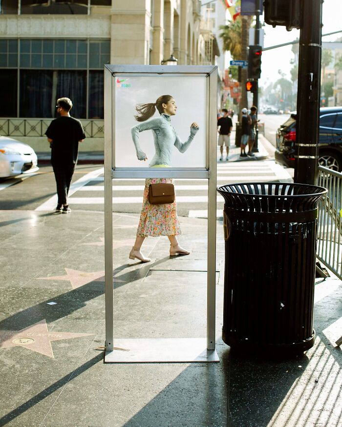 Perfectly timed street photo by Jeremy Paige of a woman's legs appearing to run beneath a Nike ad poster.