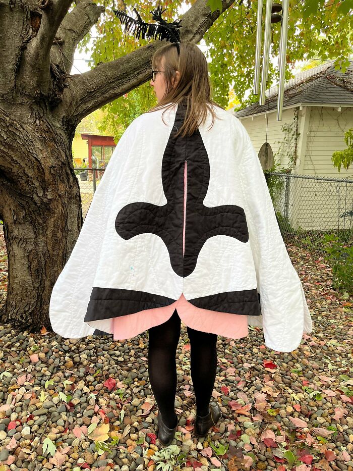 Person wearing black and white cape with fleur-de-lis design standing under tree