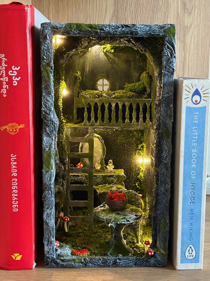 A handmade mossy forest book nook diorama with warm lights and miniature mushrooms sandwiched between books.
