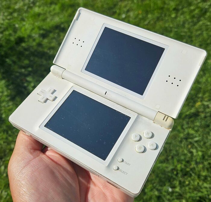 A person holding a classic white Nintendo DS Lite console, unique thrift store finds