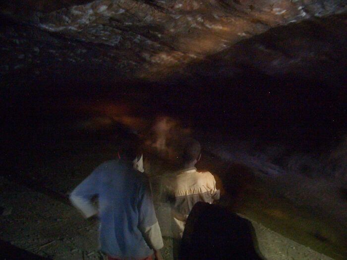 Two figures exploring a dark cave lit by faint light, resembling a real-life horror movie shot