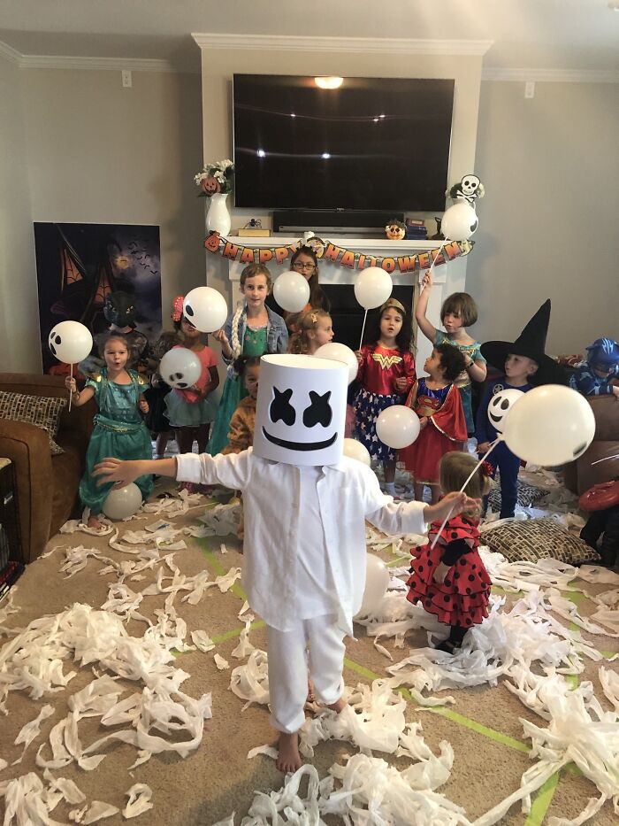 Group of children wearing various Halloween costumes during a party with a Marshmello mask in the foreground.