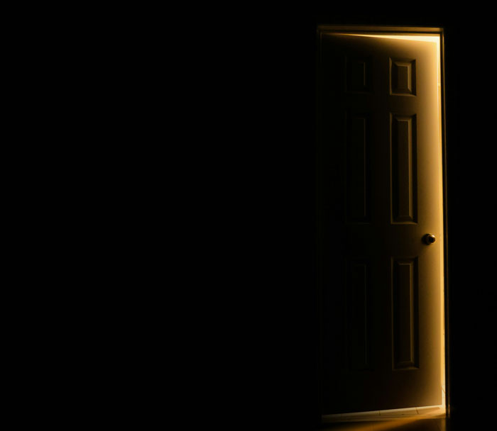 A glowing light shining through an open door in a pitch black room, reminiscent of spooky Halloween stories.