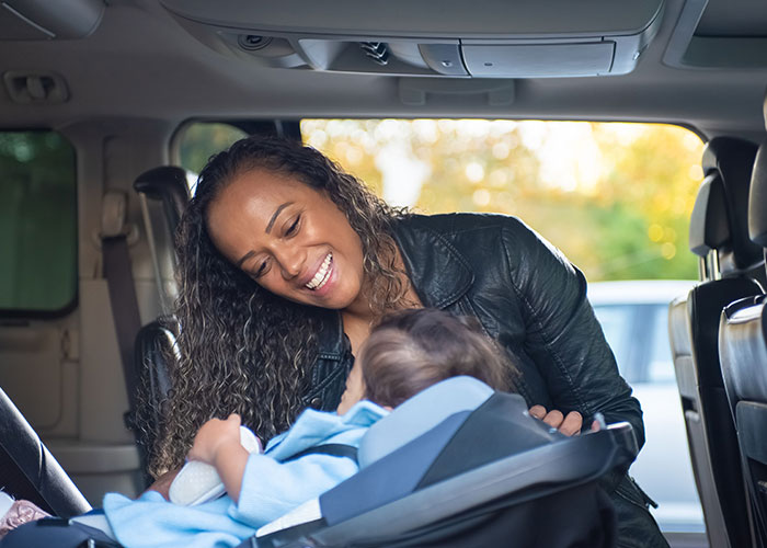 A smiling mother checking on her baby in a car seat, experiencing new motherhood.