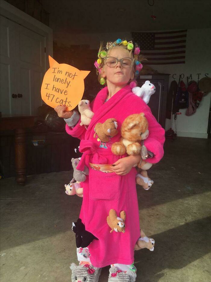 A young child in a pink robe covered with plush toy cats for a creative kids Halloween costume.